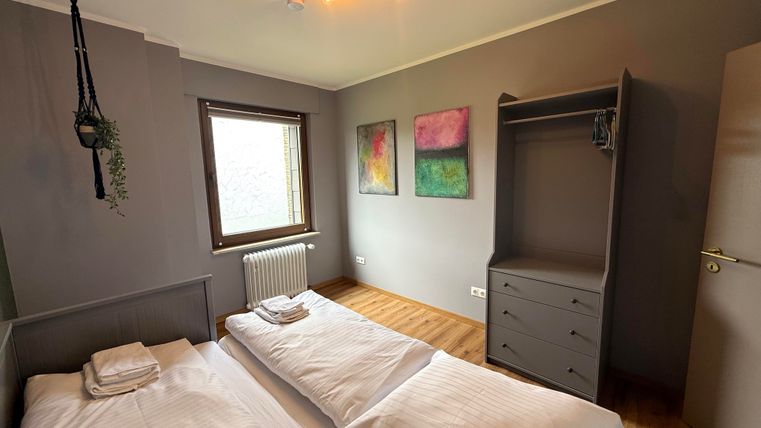 Ein gemütliches Schlafzimmer mit zwei Einzelbetten und einem Holzfußboden. Die Wände sind grau, dekoriert mit modernen Bildern, und es gibt einen Kleiderschrank sowie ein Fenster für Tageslicht.