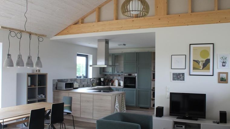Ein modernes Wohnzimmer mit offener Küche. Die Einrichtung ist hell und stylish, mit einem großen Esstisch und gemütlichen Sitzgelegenheiten.