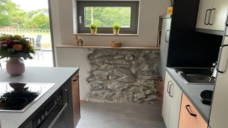 Eine moderne Küche mit einem gemischten Design aus Holz und Stein. Durch das Fenster ist ein grüner Ausblick sichtbar.