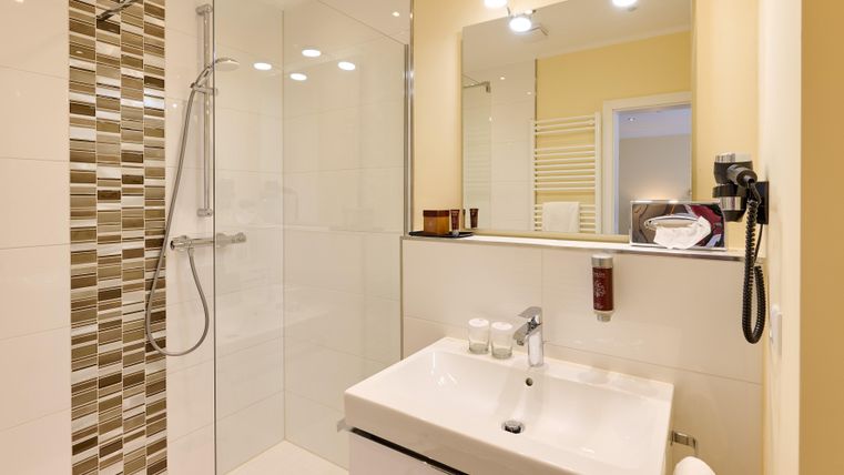 Ein modernes Badezimmer mit einer gläsernen Dusche und einem eleganten Waschtisch. Die Wände sind hell und die Fliesen haben ein stilvolles Muster.
