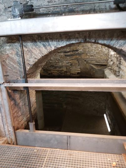 Eine steinerne Öffnung mit einem Geländer, das in einen dunklen Raum führt. Es sind Wände aus Naturstein zu sehen.