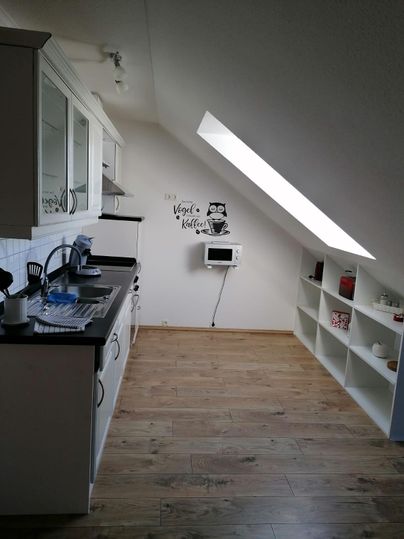 Eine moderne Küche unter dem Dach mit Holzfußboden. Sie enthält Küchenmöbel, einen Mikrowellenherd und einen kleinen Essbereich.