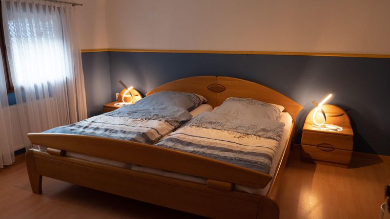 Ein gemütliches Schlafzimmer mit einem Doppelbett und Nachtkästchen. Die Wände sind blau gestrichen, und sanftes Licht strahlt von den Lampen.