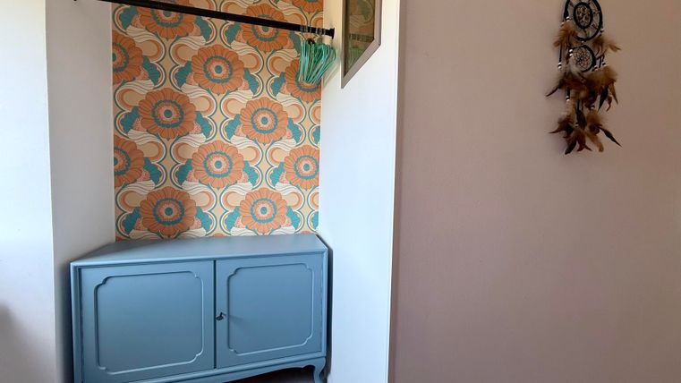 Ein stilvoller Flur mit einer blauen Kommode und buntem, floralen Tapetenmuster. An der Wand hängt ein Traumfänger.