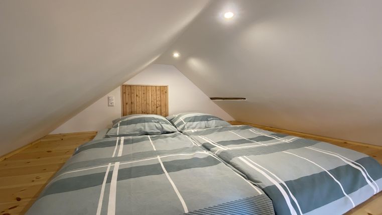 Ein gemütliches Schlafzimmer im Dachgeschoss mit einem Doppelbett und hellen Wänden. Die Bettwäsche hat ein modernes, gestreiftes Muster.