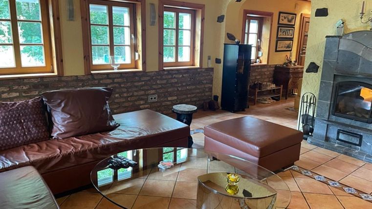 Ein gemütliches Wohnzimmer mit einem braunen Sofa und einem gläsernen Tisch. Der Raum hat große Fenster und eine warme, einladende Atmosphäre.