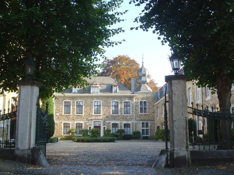 Ein elegantes Gebäude mit großen Fenstern und einem schönen Garten. Der Eingang wird von hohen Bäumen gesäumt.