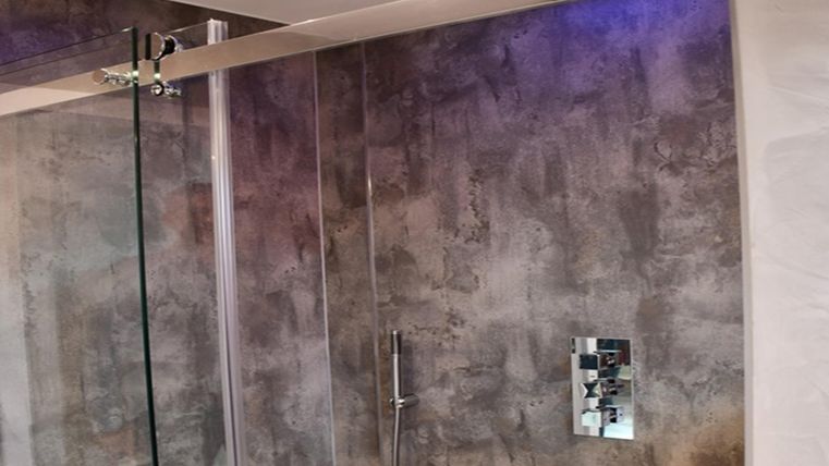 Ein modernes Badezimmer mit einer Glasdusche und stylishen Betonwänden. Die Beleuchtung an der Decke sorgt für eine angenehme Atmosphäre.