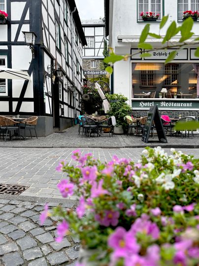 Eine malerische Gasse mit Fachwerkhäusern und gemütlichen Außenbereich. Bunte Blumen in der Vordergrund setzen einen schönen Akzent.