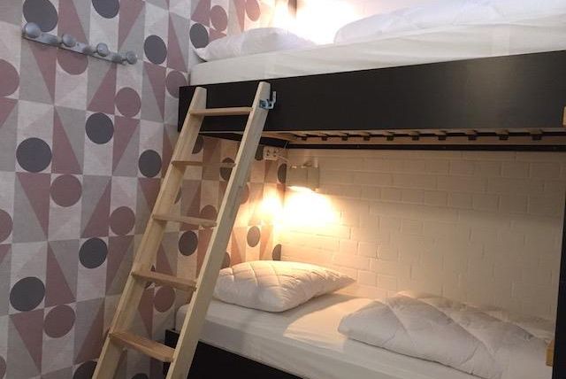 Ein gemütliches Schlafzimmer mit einem Etagenbett und einer Holzleiter. Die Wände sind mit einem modernen, geometrischen Muster dekoriert.