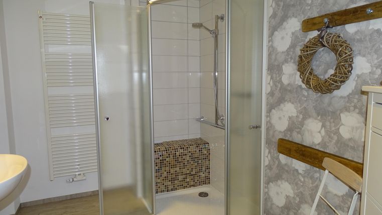 Ein modernes Badezimmer mit einer Glas-Dusche und hellen Fliesen. An der Wand hängt ein dekorativer Kranz aus Naturmaterialien.