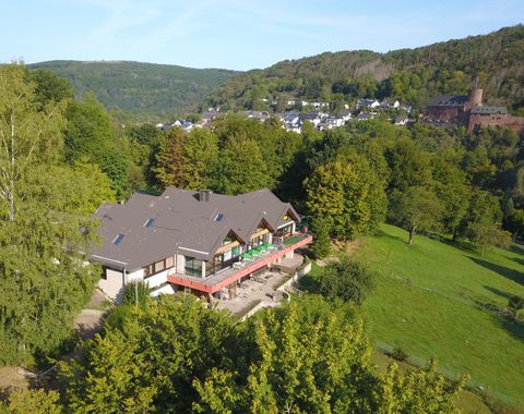 Ein gemütliches Hotel umgeben von grünen Bäumen und sanften Hügeln. Im Hintergrund sind Häuser und eine Burg sichtbar.