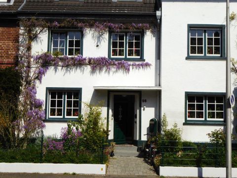 Ein charmantes Haus mit weißen Wänden und grünen Fensterrahmen. Bunte Pflanzen, besonders lila Blüten, schmücken die Fassade und den Garten.