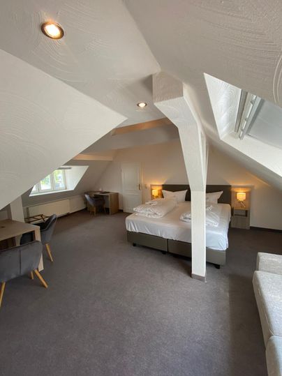 Ein gemütliches Zimmer im Dachgeschoss mit zwei Betten, einem Schreibtisch und einem Fenster. Die Wände sind weiß und die Beleuchtung ist angenehm.