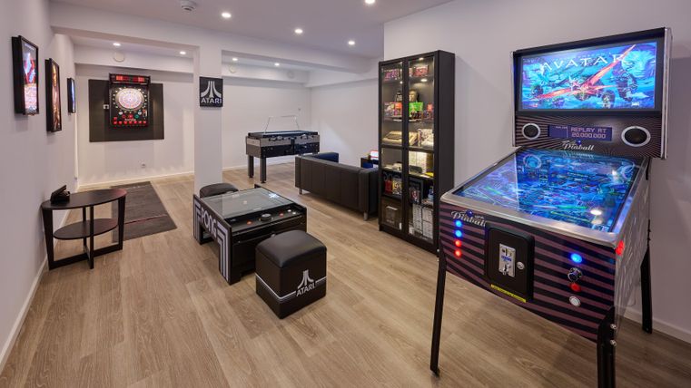 Ein moderner Spielraum mit verschiedenen Arcade-Spielen und einem Flipperautomaten. Die Wände sind mit Kunstwerken dekoriert, und es gibt bequeme Sitzgelegenheiten.