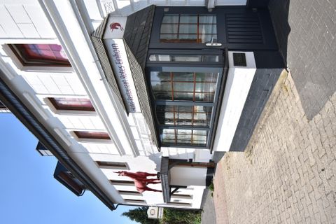 Ein charmantes Gebäude mit einem markanten Eingang. Die Fassade ist weiß und hat rote Fensterrahmen.