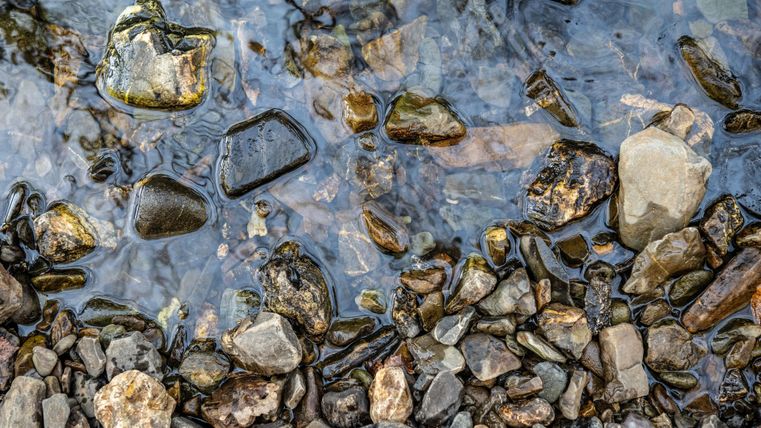Ein klarer Wasserfluss, der über runde Steine fließt. Die verschiedenen Steine haben unterschiedliche Farben und Texturen.