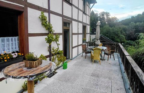 Eine gemütliche Terrasse mit einem Tisch und Stühlen, umgeben von Pflanzen. Im Hintergrund ist eine grüne Landschaft zu sehen.