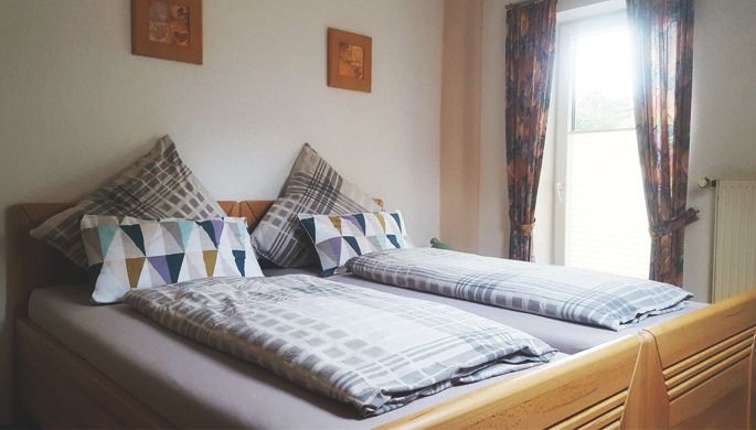 Ein gemütliches Schlafzimmer mit zwei Einzelbetten und bunten Kissen. Das Fenster lässt viel Tageslicht herein und die Vorhänge sind farbenfroh.