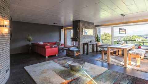 Ein modernes Wohnzimmer mit rotem Sofa und großem Esstisch. Große Fenster bieten eine Aussicht auf die Natur.