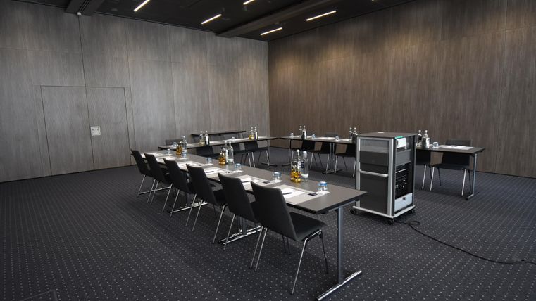 Ein moderner Konferenzraum mit mehreren Tischen und Stühlen. Die Wände sind dunkel und die Beleuchtung ist indirekt.