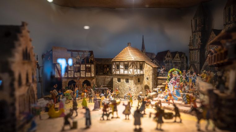Eine detailreiche Miniaturszene mit einem Dorf und Figuren, die eine festliche Atmosphäre schaffen. Das Bild zeigt historische Gebäude und fröhliche Menschen inmitten von Aktivitäten.