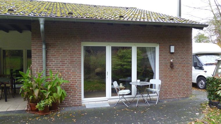 Ein modernes Haus mit einer Terrasse. Es gibt einen kleinen Tisch mit Stühlen und einige Pflanzen.