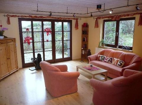 Ein gemütliches Wohnzimmer mit rosa Sesseln und einem Tisch in der Mitte. Große Fenster bieten einen Blick auf den Garten.