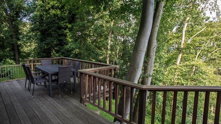 Eine gemütliche Terrasse aus Holz mit einem Tisch und Stühlen, umgeben von Bäumen. Der Blick auf die grüne Natur schafft eine entspannende Atmosphäre.