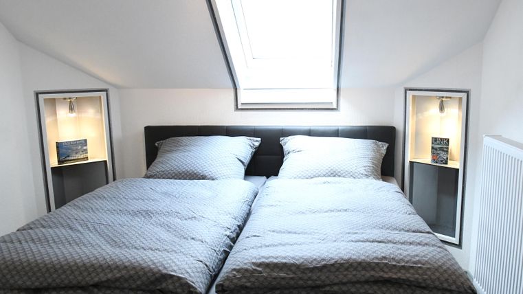 Ein helles Schlafzimmer mit zwei zusammengestellten Betten. Es gibt Dachfenster und moderne Nachttische mit Beleuchtung.