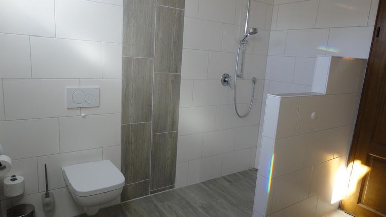 Ein modernes Badezimmer mit einer Dusche und WC. Die Wände sind weiß gefliest, und der Boden hat graue Fliesen.