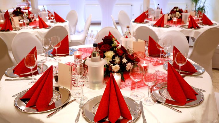 Ein festlich dekorierter Tisch mit roten Servietten und eleganten Gläsern. Blumenarrangements und Kerzen schaffen eine einladende Atmosphäre.