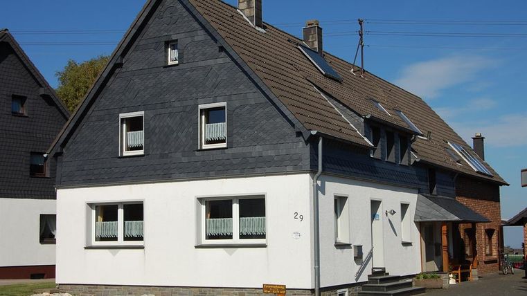 Ein modernes zweigeschossiges Haus mit einer Kombination aus schwarzer und weißer Fassade. Die Fenster sind hell und die Dachziegel sind braun.