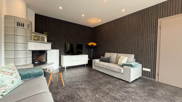 Ein modernes Wohnzimmer mit gemütlichen Sofas und einem Kamin. Die Wände sind dunkel gestreift, und es gibt eine Fernsehecke.