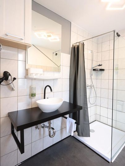 Ein modernes Badezimmer mit einem Glasduschbereich und einer eleganten Waschtischanordnung. Die Wände sind mit weißen Fliesen gefliest und ein Spiegel reflektiert den Raum.