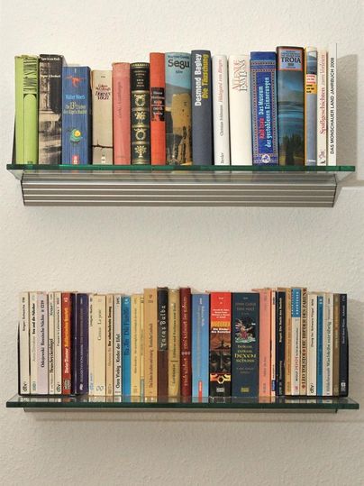 Zwei Bücherregale mit einer Vielzahl von Büchern in verschiedenen Farben. Das obere Regal hat größere, gebundene Bücher, während das untere Regal vorwiegend Taschenbücher enthält.