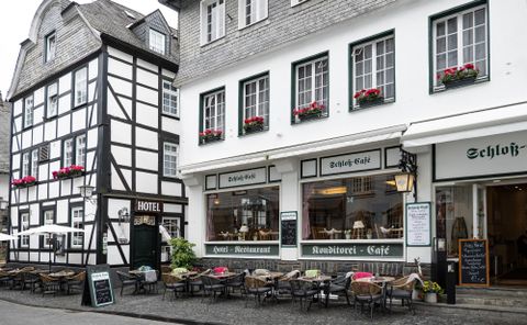 Ein malerisches Stadtbild mit traditionellen Häusern und einem einladenden Café. Auf der Straße stehen Tische und Stühle, die zu einem gemütlichen Aufenthalt einladen.
