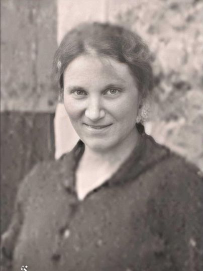 Ein schwarz-weißes Porträt einer Frau mit einem sanften Lächeln. Sie trägt einen dunklen Pullover und hat lockiges Haar.
