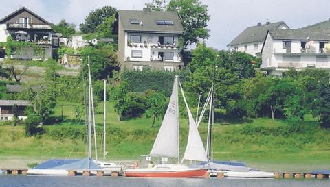 Ein ruhiger Wasserbereich mit mehreren Segelbooten im Vordergrund. Im Hintergrund sind grüne Wiesen und einige Häuser zu sehen.