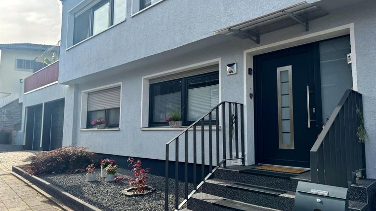 Ein modernes Haus mit einem klaren, minimalistischen Design. Der Eingangsbereich hat eine große Haustür und ist von einem Gehweg umgeben.
