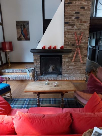 Ein gemütliches Wohnzimmer mit einem Kamin und roten Sofas. Der Raum hat eine rustikale Atmosphäre mit Holzelementen und einer modernen Wanddekoration.