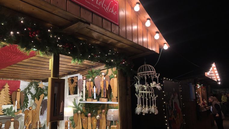 Ein geschmückter Weihnachtsstand in der Nacht, beleuchtet von warmem Licht. Es gibt Holzornamente und festliche Dekorationen zu sehen.