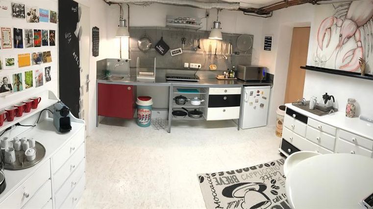 Eine moderne Küche mit Edelstahlgeräten und vielen Schränken. An der Wand hängen Bilder und Postkarten, die dem Raum eine kreative Note verleihen.
