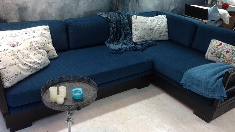 Ein gemütliches blaues Sofa mit dekorativen Kissen und einer Decke. Neben dem Sofa steht ein kleiner Tisch mit Kerzen.