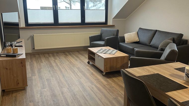 Ein modernes Wohnzimmer mit einem grauen Sofa und einem Holzkaffee Tisch. Große Fenster sorgen für viel Licht und einen Blick nach draußen.