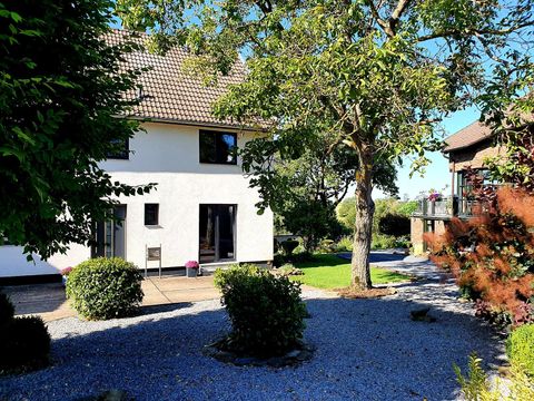 Ein modernes Haus umgeben von einem gepflegten Garten. Bäume und Sträucher verleihen der Umgebung eine angenehme Atmosphäre.