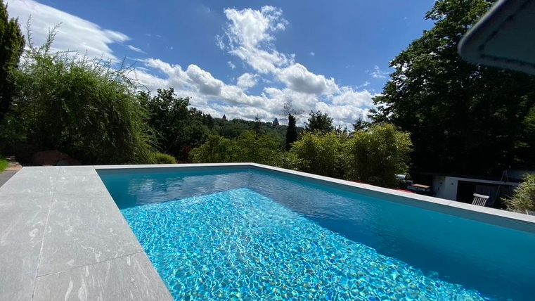 Ein schöner Pool mit klarem, blauem Wasser. Im Hintergrund sind grünes Laub und ein strahlend blauer Himmel zu sehen.