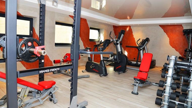 Ein modernes Fitnessstudio mit roten Geräten und einer hellen, einladenden Atmosphäre. Die Wände sind in warmen Tönen gestaltet und sorgen für eine motivierende Umgebung.