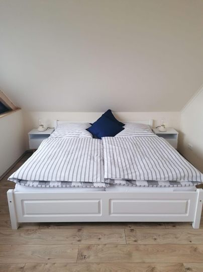 Ein gemütliches Schlafzimmer mit einem großen Bett und gestreiften Bettdecken. Neben dem Bett stehen zwei Nachttische mit Lampen.