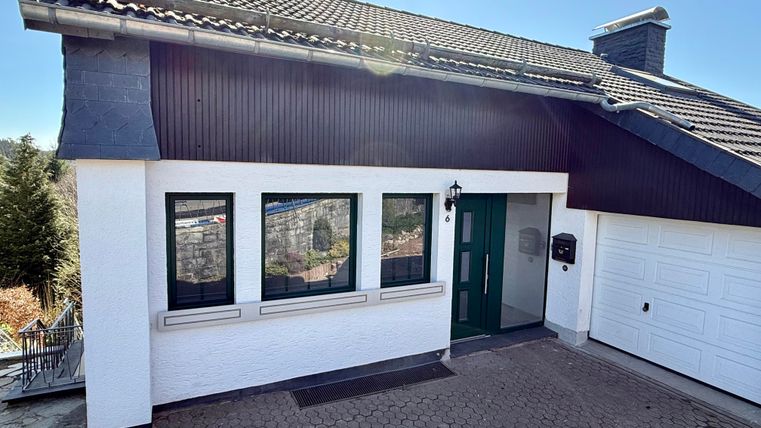 Ein modernes Einfamilienhaus mit einem begrünten Eingangsbereich. Die Fassade ist hell gestrichen und hat große Fenster.